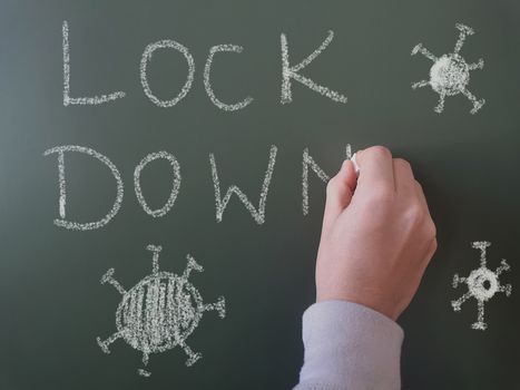 Hand drawing the word lockdown on chalkboard with chalk, symbolizing pandemic impact.