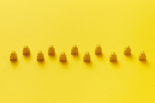 A row of yellow meeple pieces on a vibrant yellow background, showcasing uniformity and pattern.