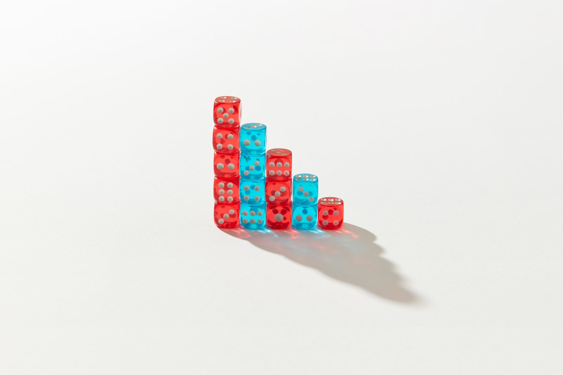 A creative arrangement of red and blue dice stacked in a descending pattern casting a shadow.