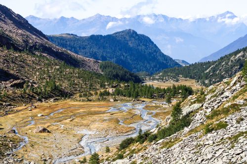 Free A stunning view of a mountain valley with a winding stream under a clear blue sky. Stock Photo