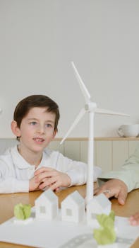 A young boy learns about renewable energy using a wind turbine model in a classroom setting.