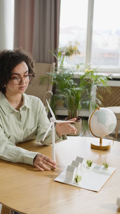Free Woman with curly hair examines a model wind turbine for a school project indoors. Stock Photo