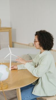 Woman sitting at a table interacting with a wind turbine model and globe, symbolizing education and sustainability.
