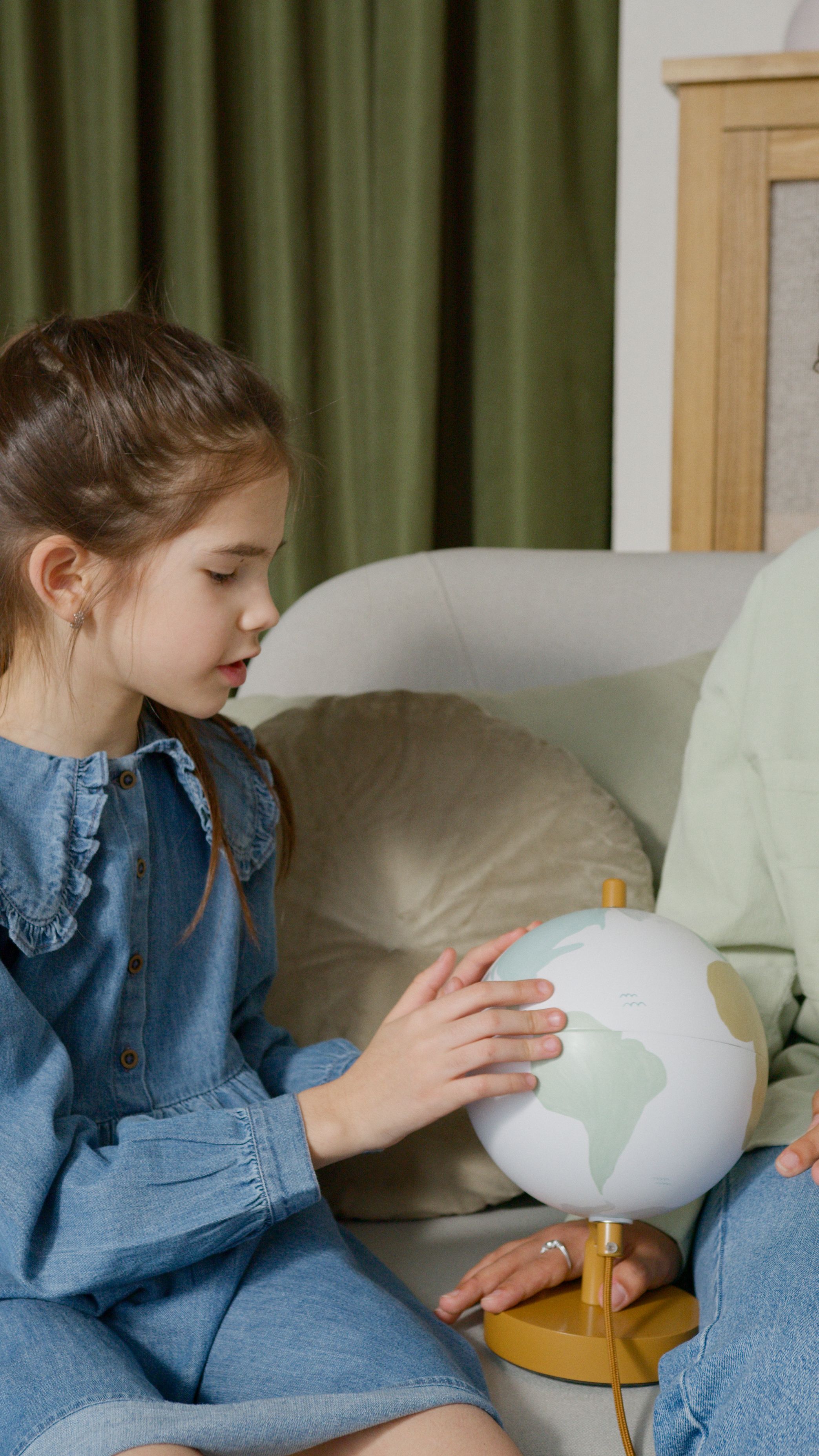 Young girl sitting on a couch, exploring a globe in a cozy indoor setting.