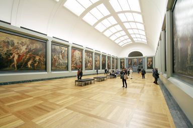 A long museum hall densely hung with gilt-framed paintings