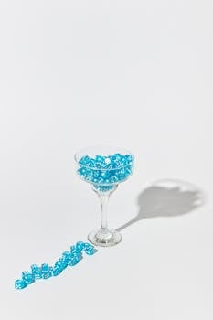 A cocktail glass filled with blue dice casting a distinct shadow on a white background.