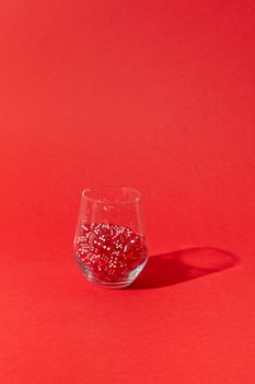 A clear glass filled with red dice set against a vibrant red background, creating a bold aesthetic.