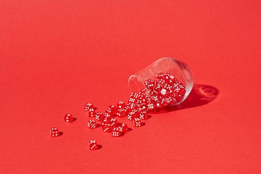 Red dice spilling from a glass on a bright red background, capturing a playful and dynamic scene.