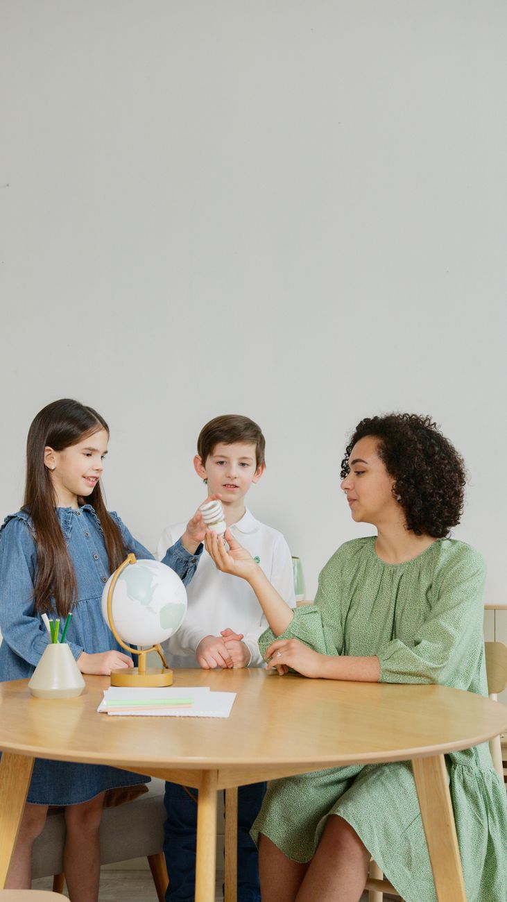 Duas crianças e um professor participando de uma aula ecológica com um globo e um modelo de turbina eólica.