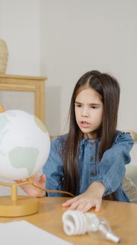 Young girl in denim studies globe indoors, emphasizing education and curiosity.