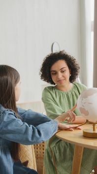 A woman and a girl engaging in learning with a globe at a wooden table indoors.