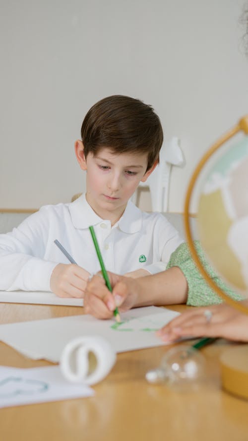 A Boy in a White Shirt Writing on a White Paper