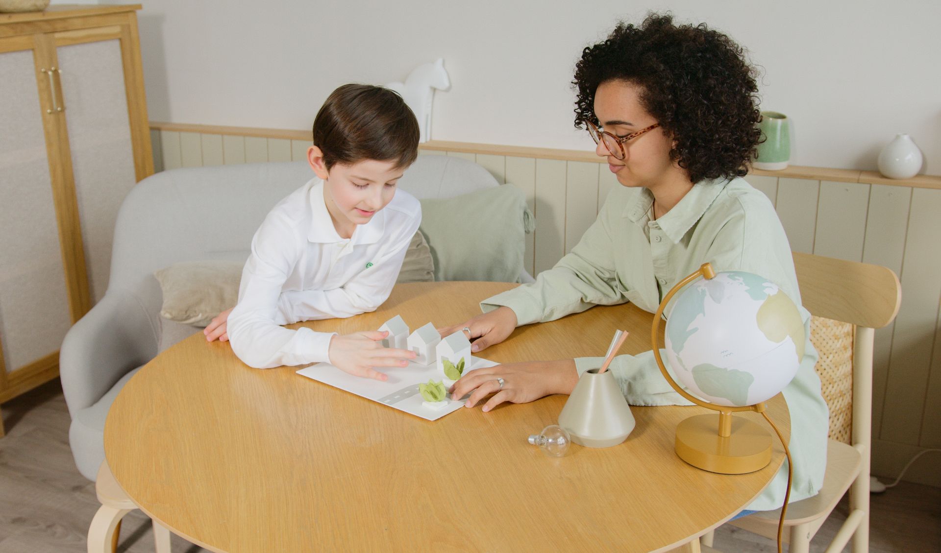 A teacher and student engage in learning with eco-friendly models in a cozy classroom setting.