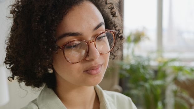Close-up portrait of a woman with curly hair and eyeglasses indoors.
