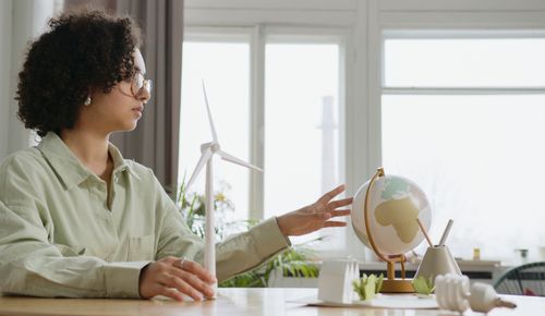 Free A young woman explores renewable energy with a globe and wind turbine model indoors. Stock Photo