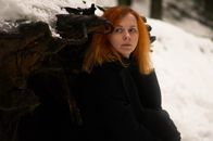 Emotionless adult female in black coat near fallen tree trunk with roots in snowy woods in winter day while looking away pensively