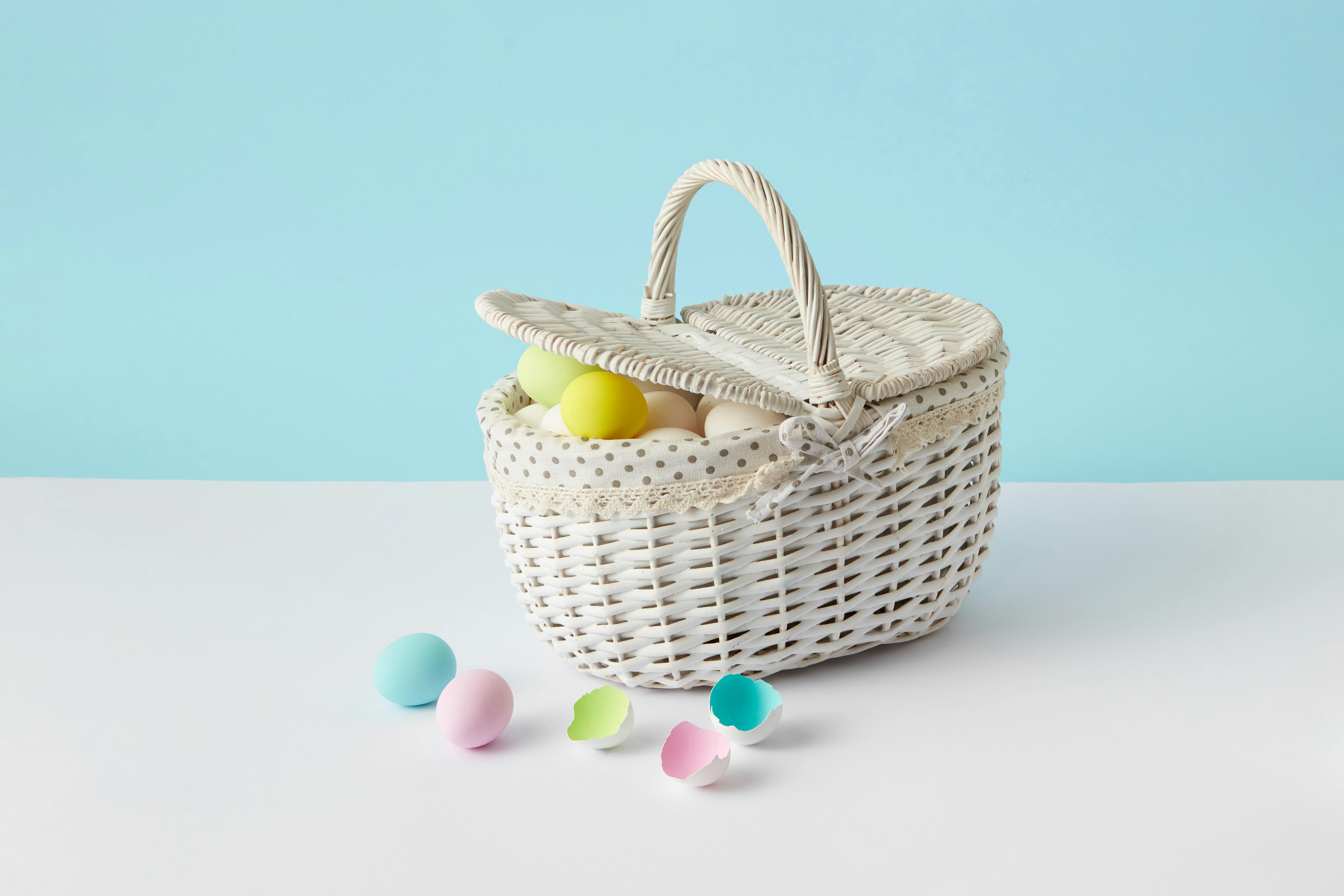 White wicker basket filled with pastel-colored Easter eggs on a light blue background.