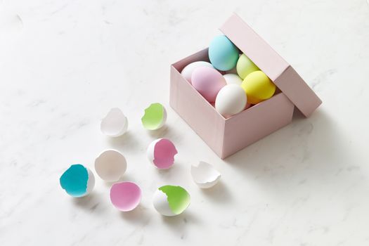 A set of pastel-colored Easter eggs displayed in a decorative box with scattered eggshells on a white surface.