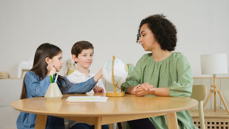 Kids Sitting Beside The Curly Haired Woman On The Wooden Table 