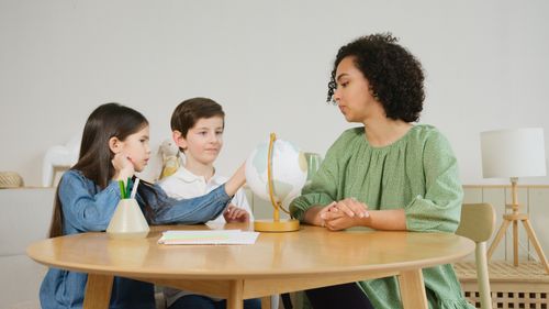 Free A teacher guides two children in a geography lesson using a globe. Stock Photo