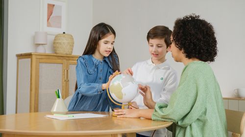 Free Children and teacher exploring globe for geography lesson indoors. Stock Photo