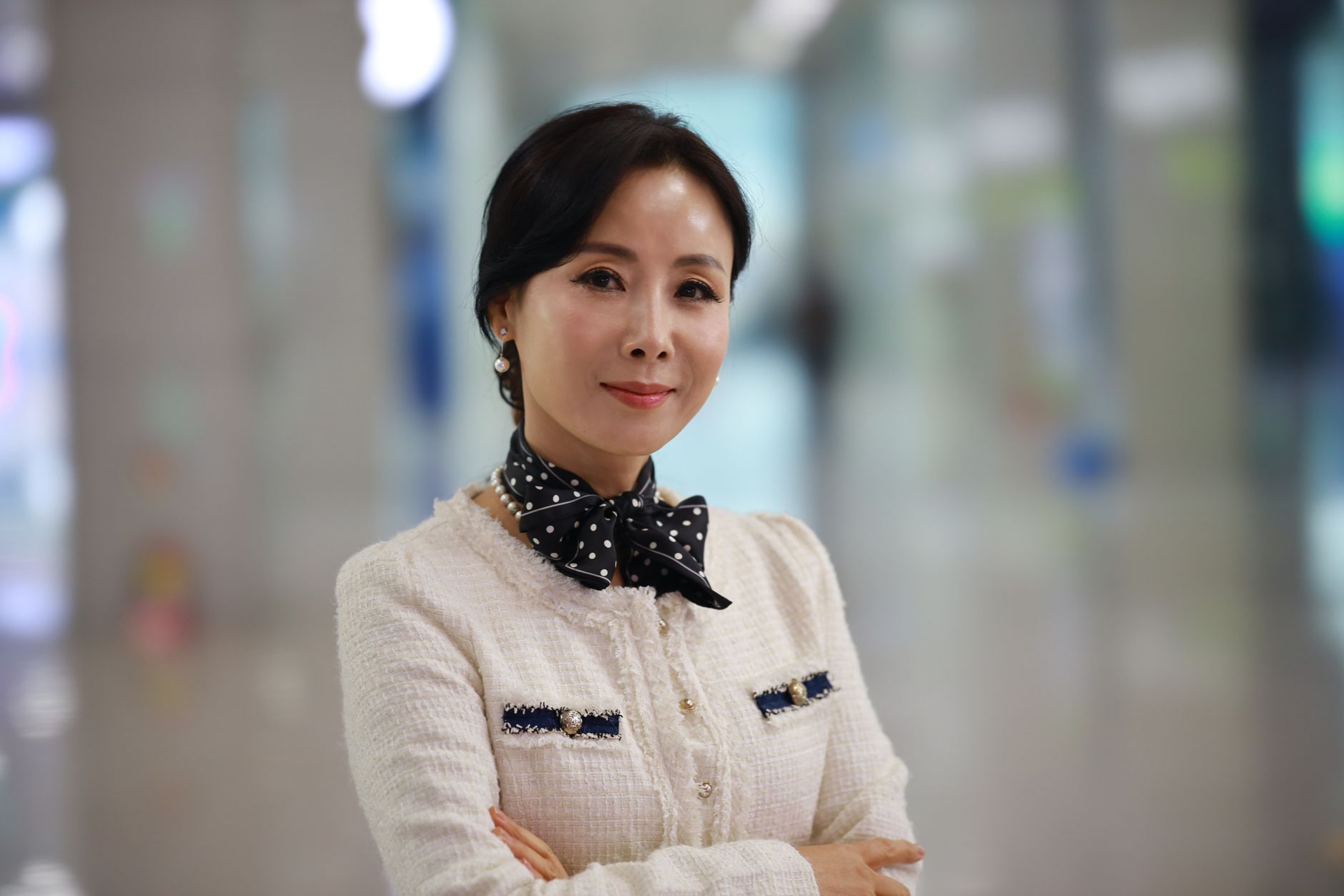 A sophisticated woman smiles confidently in a stylish outfit indoors, exuding elegance and charm.
