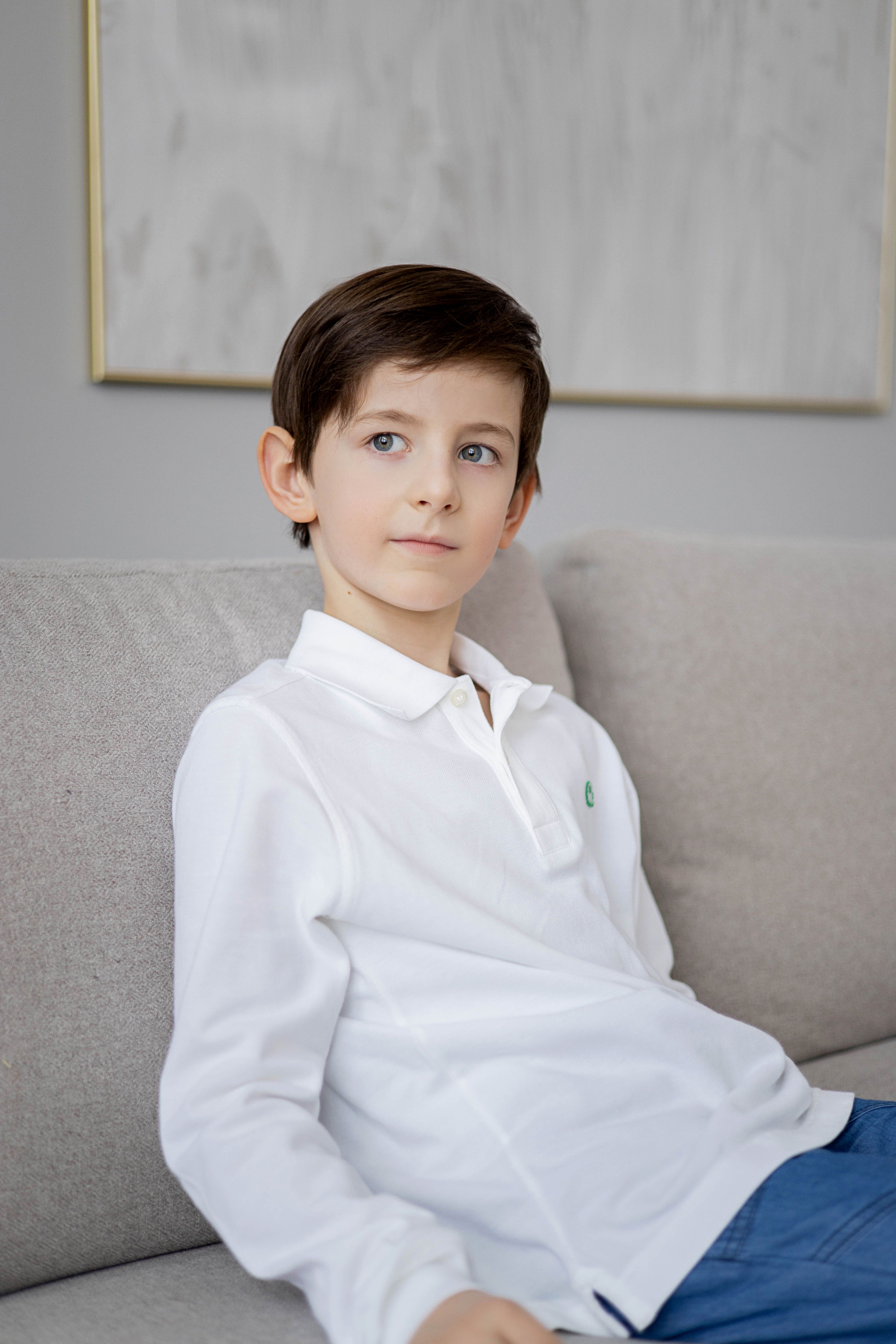 A young boy in a white shirt relaxes on a sofa in a modern living room setting.