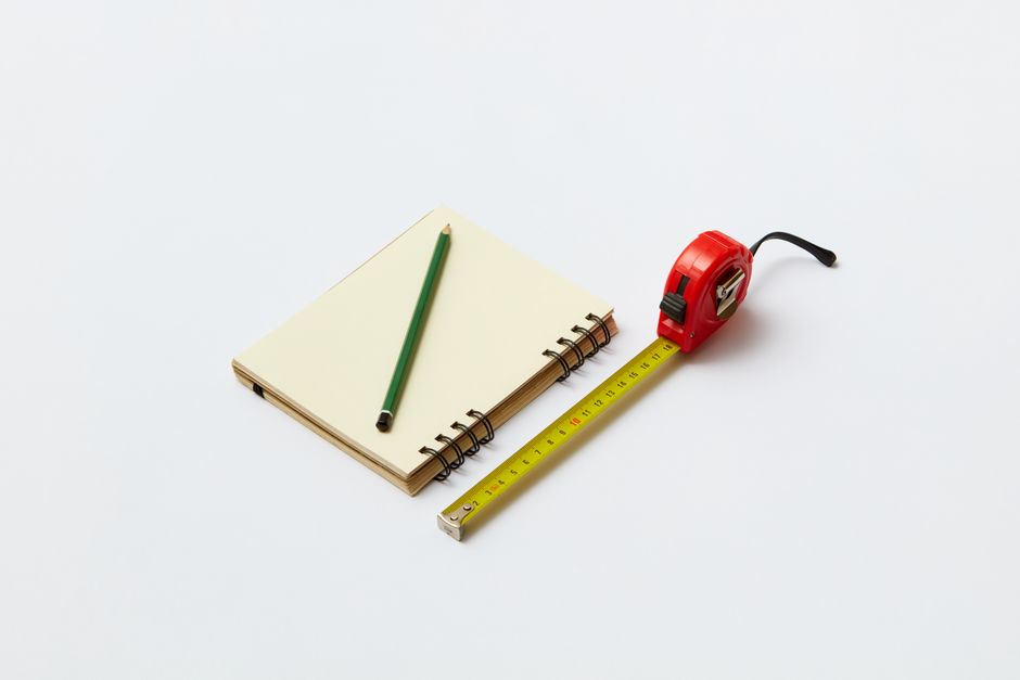 Top view of a notebook, green pencil, and measuring tape on a white background.