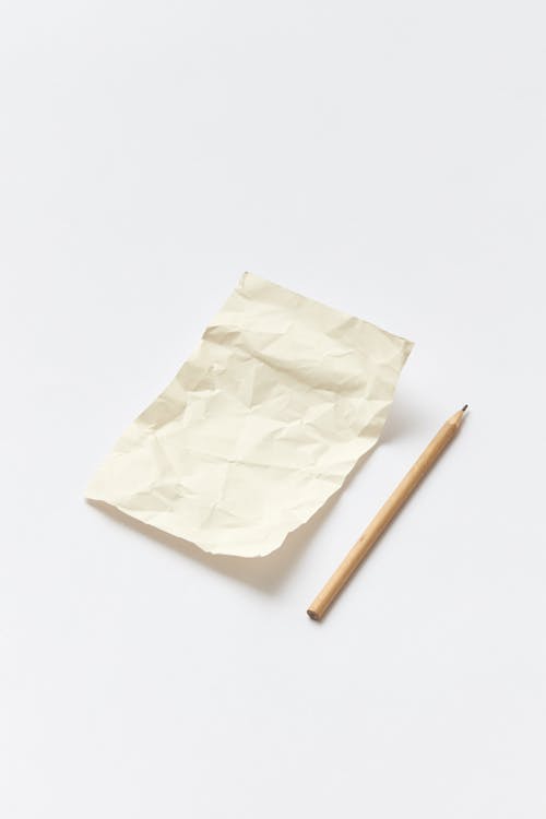 Photo of a Brown Pencil Beside a Crumpled Paper