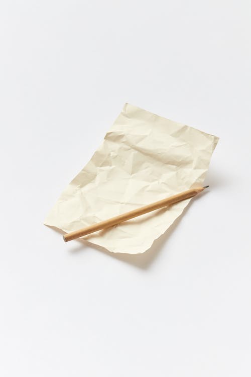 Close-Up Photo of a Brown Pencil on Top of a Crumpled Paper
