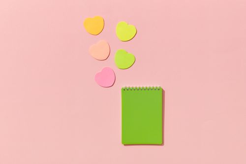 Free Vibrant heart-shaped sticky notes with a green notepad on a pink backdrop, conveying creativity and love. Stock Photo