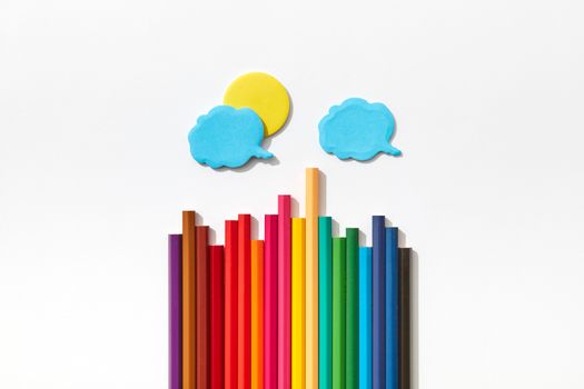 Rainbow-colored pencils arranged with cloud and sun cutouts on a white background.