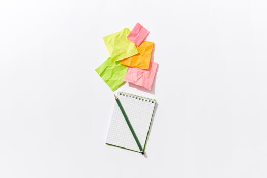 Colorful flat lay of crumpled sticky notes with a notepad and pencil on white background.