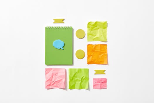 Flat lay of colorful stationery items including a green notebook and crumpled paper on a white background.