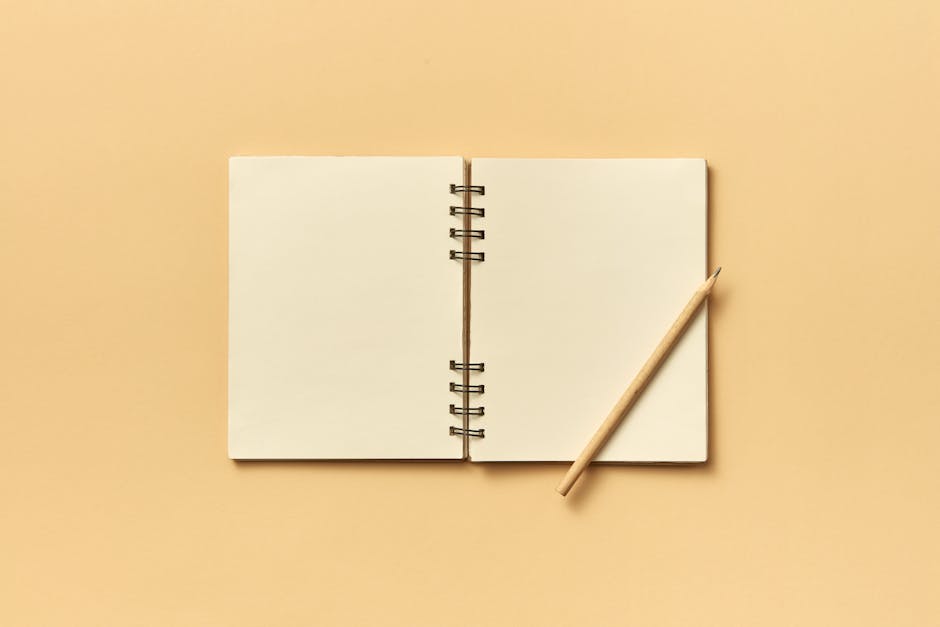 How Notion Solves Weekly YouTube Upload Planning An open spiral notebook with a pencil on a neutral beige background, perfect for creative projects and planning.