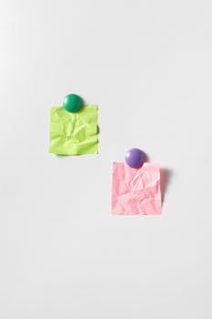 Crumpled green and pink sticky notes pinned by magnets on a white background.