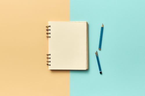 A Blank Notebook Page Beside a Broken Pencil on a Beige and Blue Surface