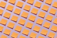 An Array of Blank Orange Notepads Stuck on Purple Surface
