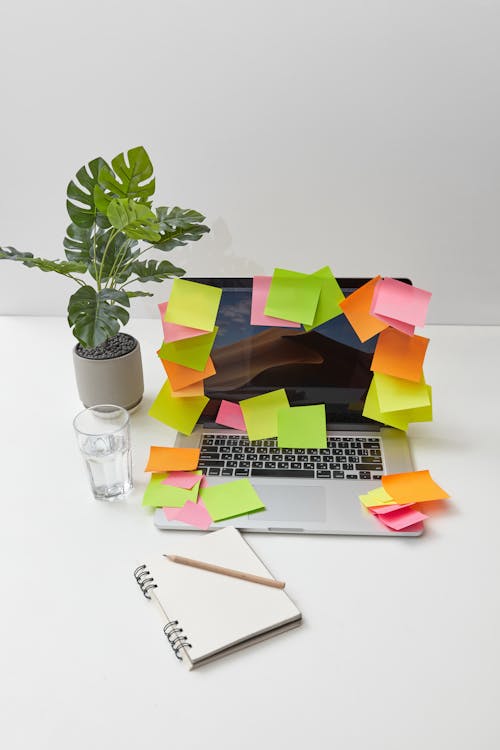 Pieces of Sticky Notes Stuck on a Laptop Beside a Notebook with Pen