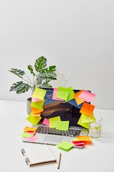 Vibrant workspace with sticky notes covering a laptop, plant, and glass on a white background.