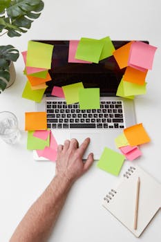 A hand reaching for a laptop surrounded by vibrant sticky notes on a tidy desk.
