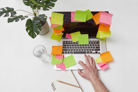 Top view of a laptop covered in sticky notes, glass of water, and monstera plant for a productive workspace feel.