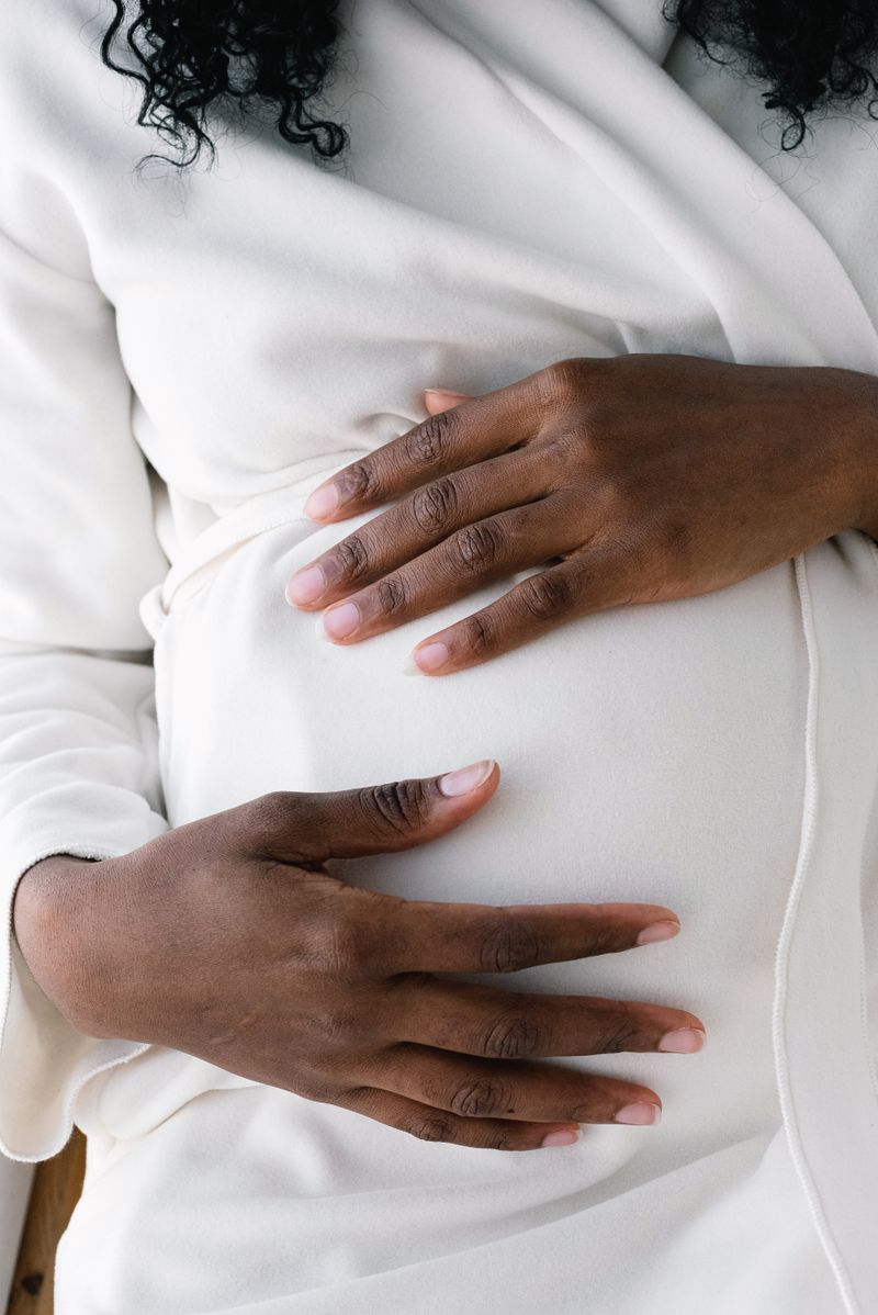 A Black pregnant woman rests both hands on her belly. Gestational diabetes rarely causes symptoms, so prenatal glucose screening is the only way most pregnancies catch it.