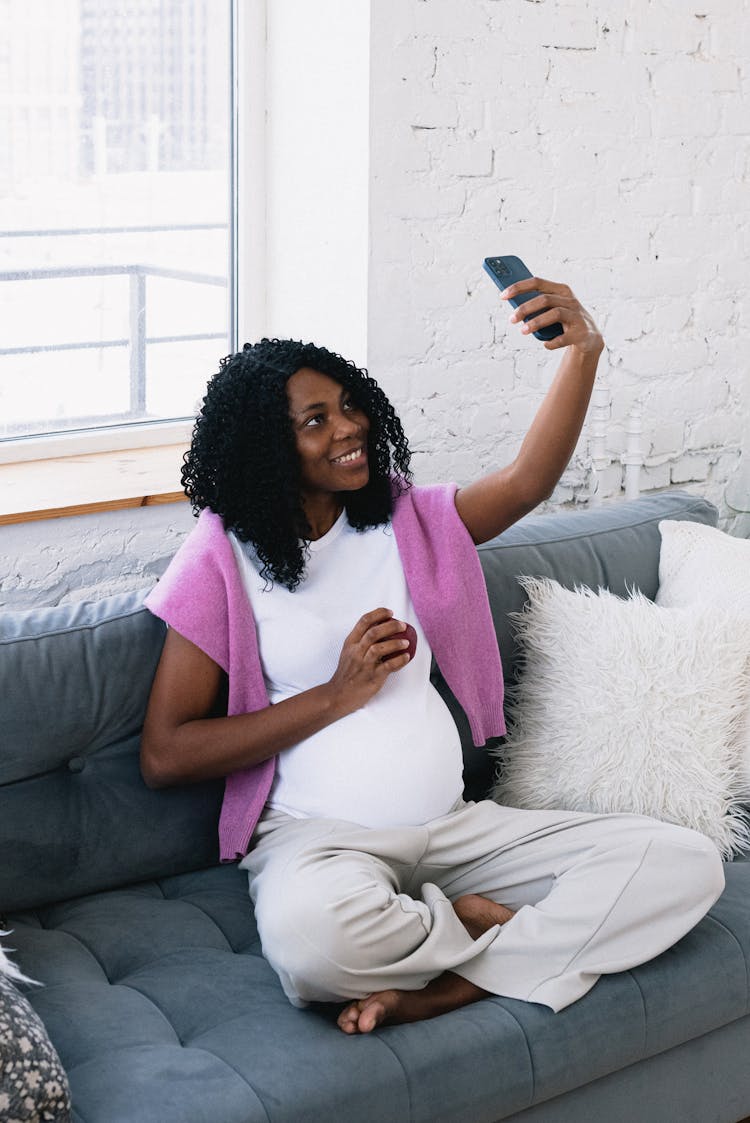 Cheerful Pregnant Black Woman Taking Selfie On Couch