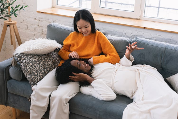 Happy Black Pregnant Woman Lying On Legs Of Asian Female