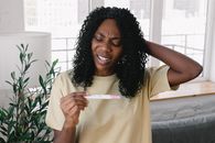 Frustrated African American female in casual clothes looking at pregnancy test in hand while standing in light living room at home