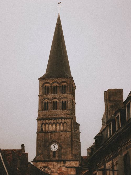 Free Low angle exterior of aged gothic church with clock near buildings under cloudless gray sky in city street in daytime Stock Photo
