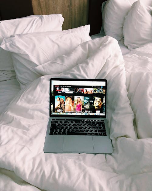 High angle of netbook with website for movie watching placed on soft duvet on cozy bed