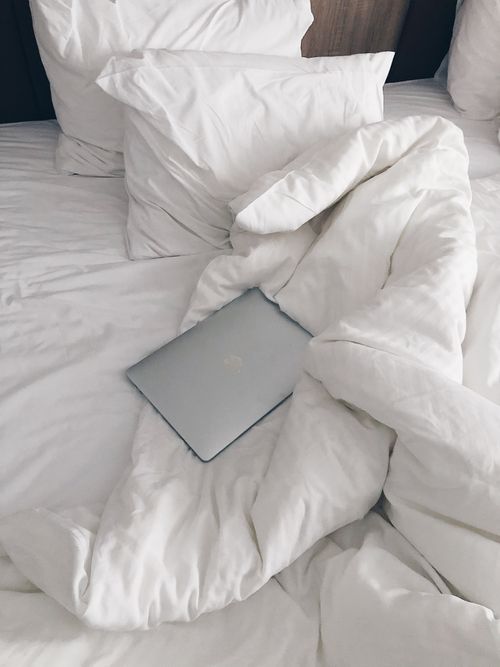 Free High angle of netbook left on cozy white duvet of bed with crumpled sheet and pillows in daylight Stock Photo