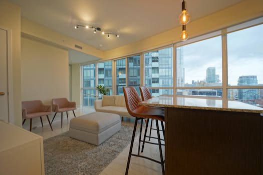 Spacious modern condominium living room featuring stylish furniture and expansive city views through large windows.